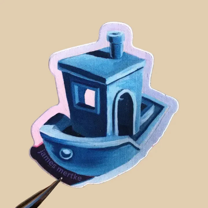 This sticker depicts a painting of Benchy, a blue tugboat used to calibrate a 3D printer.