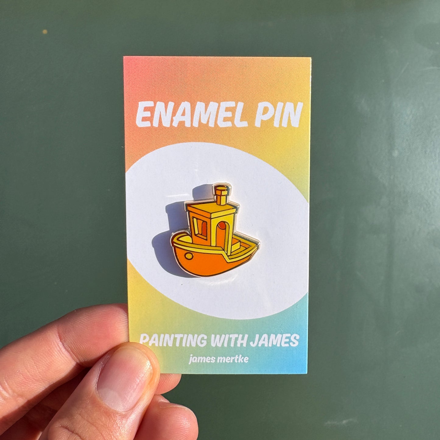 an enamel pin featuring an orange and yellow tug boat.