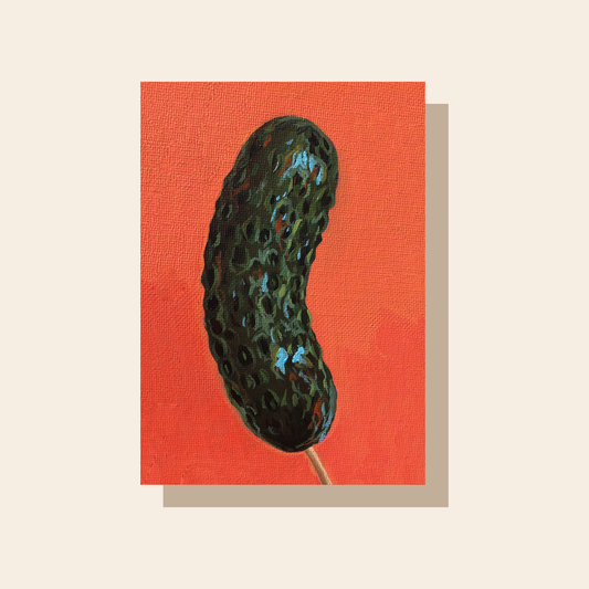 This art print features a glossy dark green pickle on a stick in front of a bright orange background.