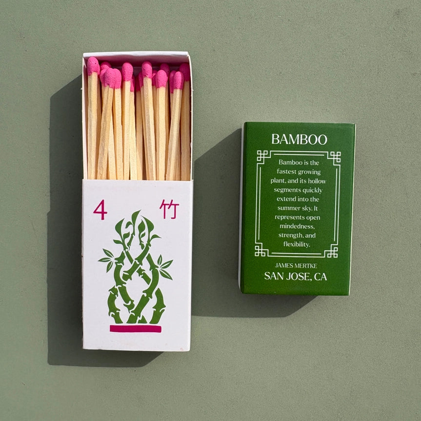 A matchbox is illustrated with a green and pink bamboo to look like a mahjong tile. There is info about the meaning of the plant on the back. Matches with pink heads are inside the box.