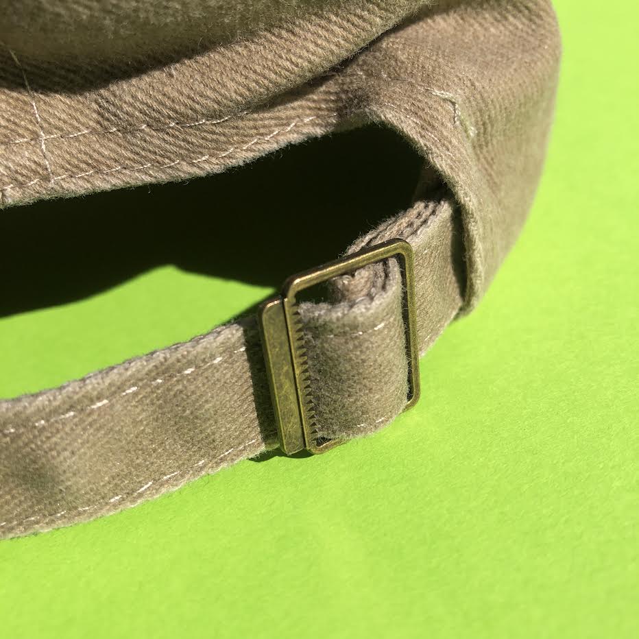 A close up on the adjustable metal buckle on the back of the hat. It allows the strap to be adjusted and for the size of the hat to change.