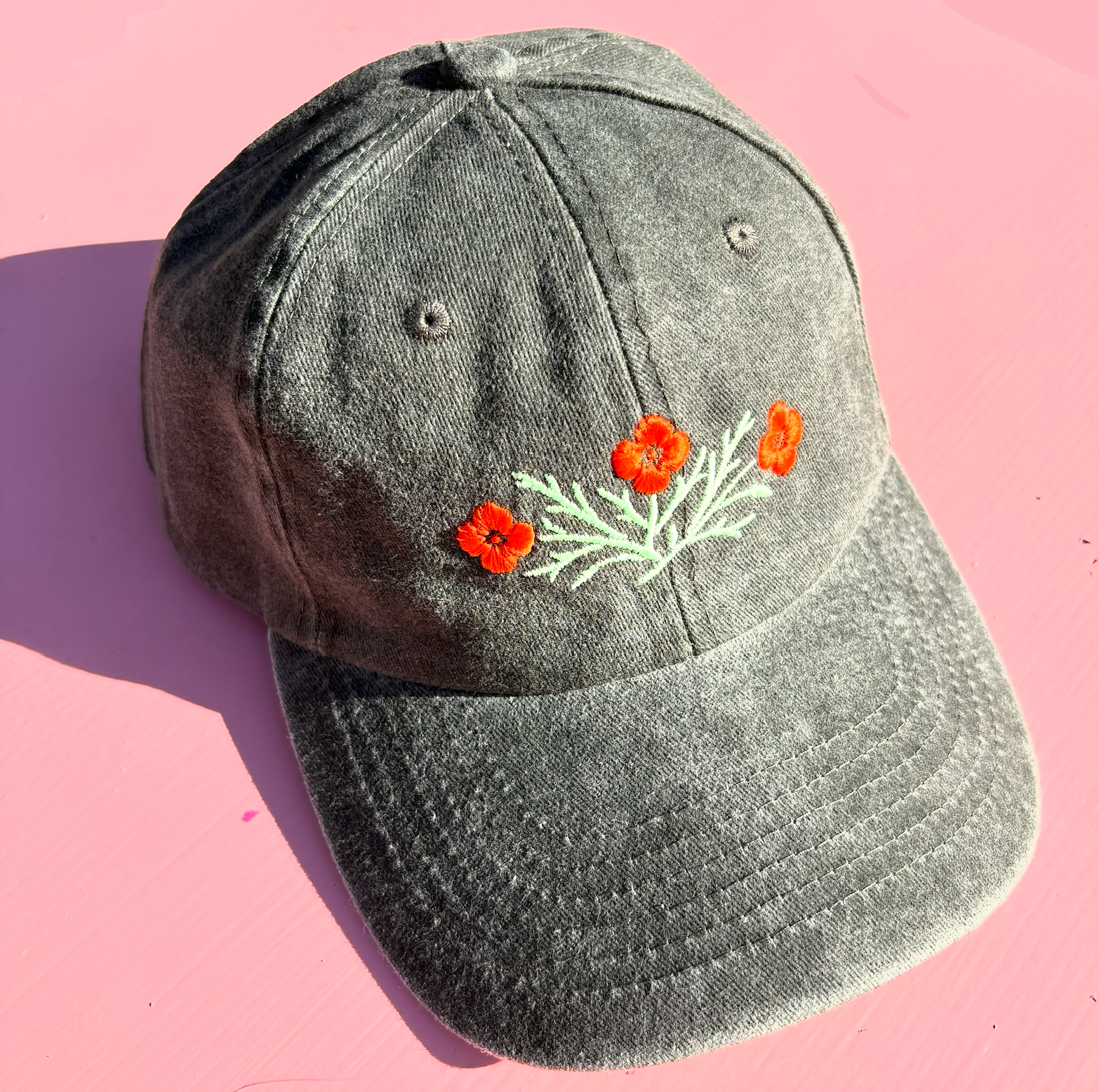 A dark grey-green washed hat embroidered with orange California poppies and light green leaves.