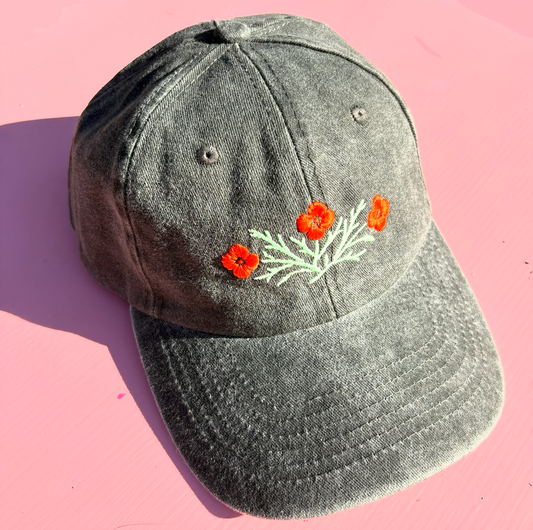 A dark grey-green washed hat embroidered with orange California poppies and light green leaves.
