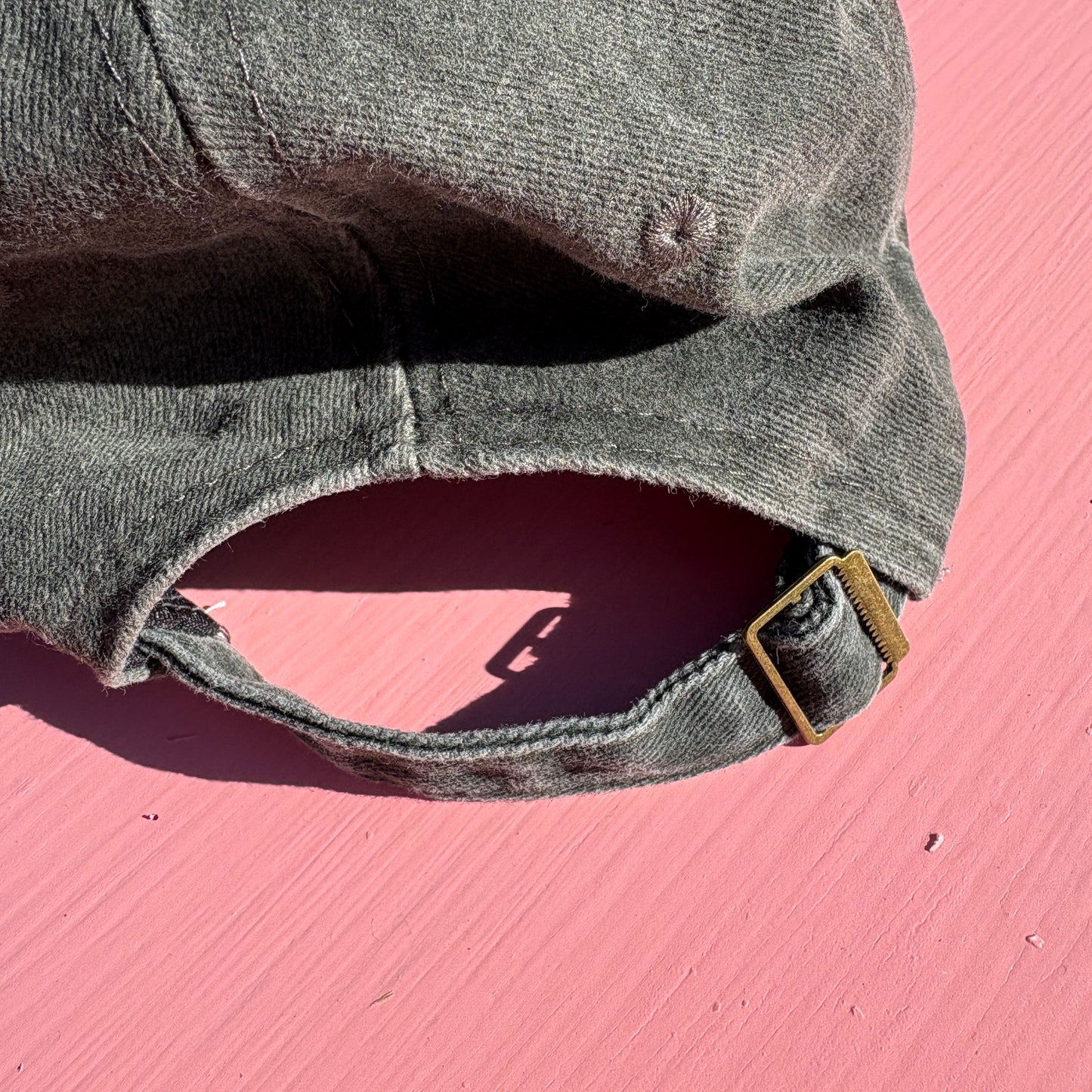 A close-up of a washed dark gray green baseball cap showing adjustable buckle on the back..