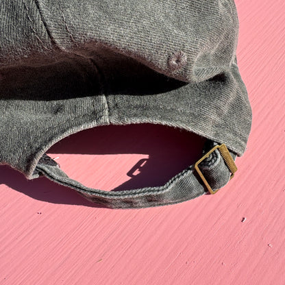 A close-up of a washed dark gray green baseball cap showing adjustable buckle on the back..
