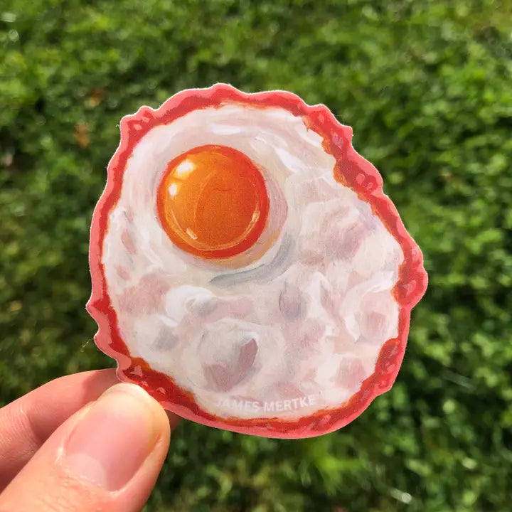 This sticker depicts a painting of a fried egg with a yellow-orange yolk and crispy edges.
