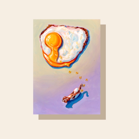 This print depicts a fried egg with a burst yolk at the top of the print and a calico cat that has tracked its yolky pay prints in the bottom half of the print.