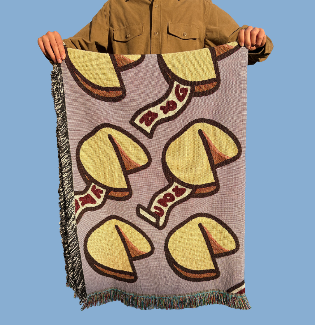 Person holding a quarter folded blanket with fortune cookie on purple pattern against a blue background