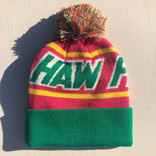 This knit beanie features a red, yellow and green design. It has a green brim and "HAW FLAKES" is written across the front in green text. A multicolored pom pom (green, yellow, white, red) is attached to the top.