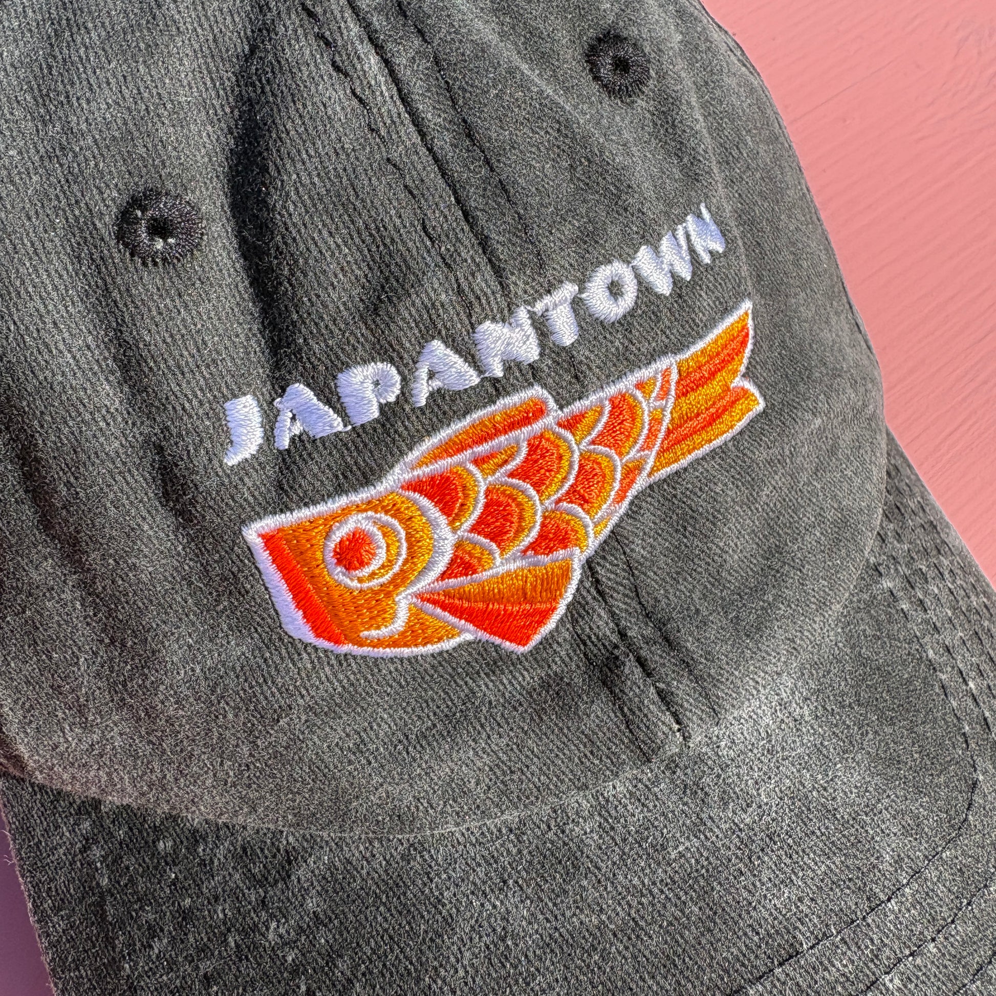A close-up of a black washed baseball cap featuring white embroidered 'JAPANTOWN' text and an orange Koinobori Carp Kite on the front.