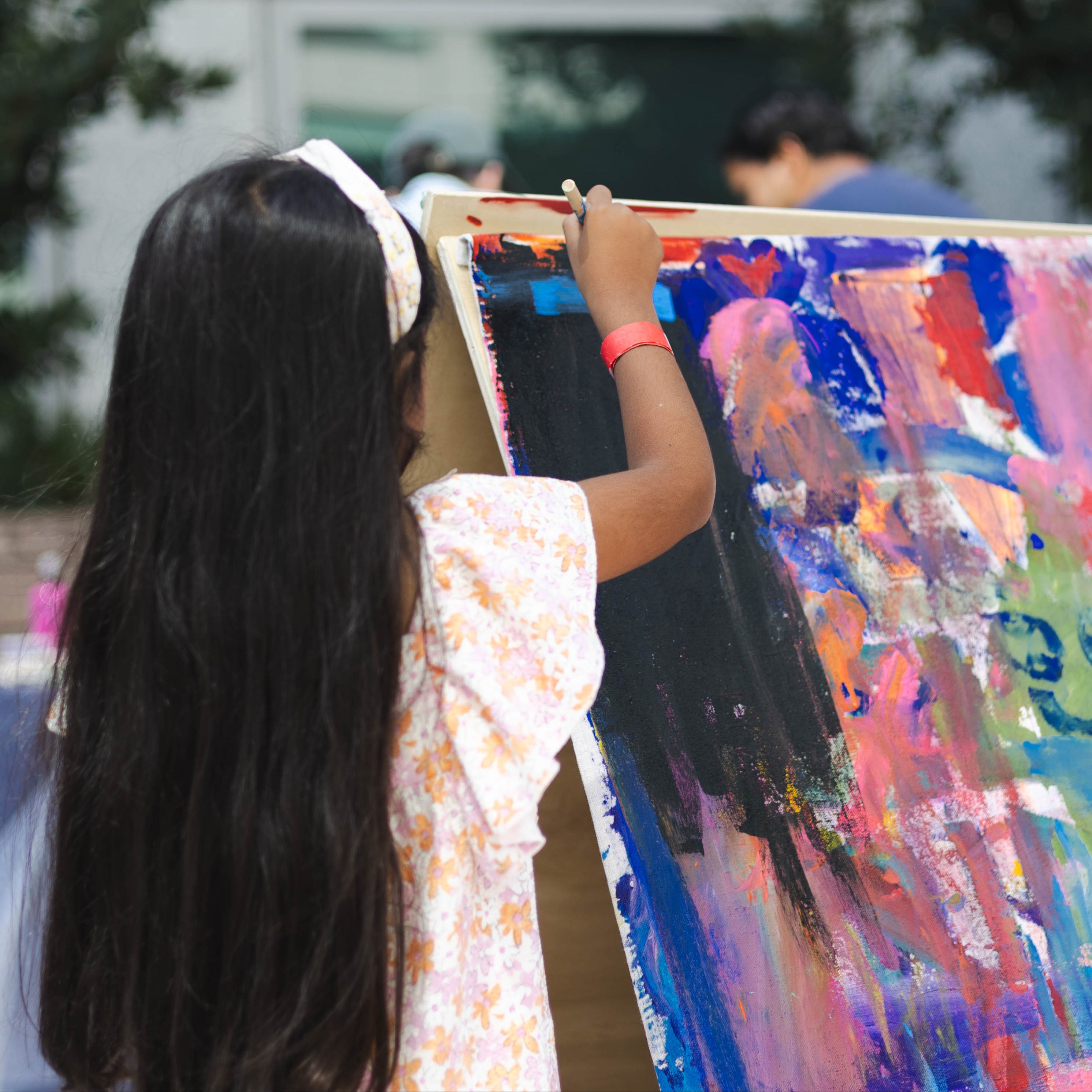 A girl with long dark hair adds her tough of color to the mural in front of her.