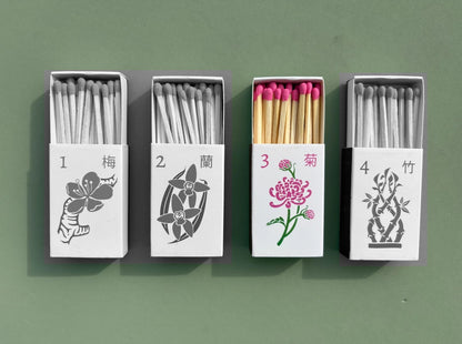 The set of four matchboxes are laid out next to each other. Only the chrysanthemum design is in color while the rest have been turned black and white to emphasize which design is included in this listing.