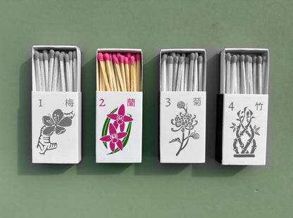 The set of four matchboxes are laid out next to each other. Only the orchid design is in color while the rest have been turned black and white to emphasize which design is included in this listing.