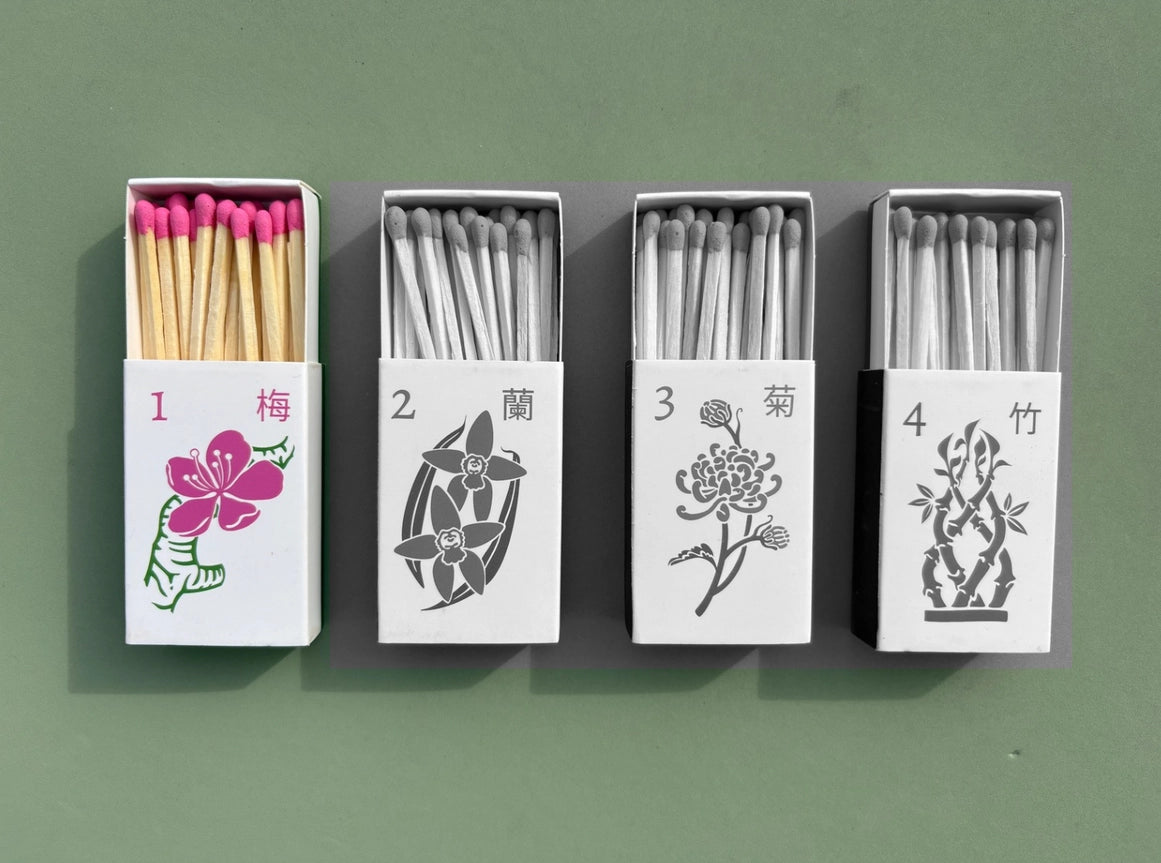The set of four matchboxes are laid out next to each other. Only the plum blossom design is in color while the rest have been turned black and white to emphasize which design is included in this listing.