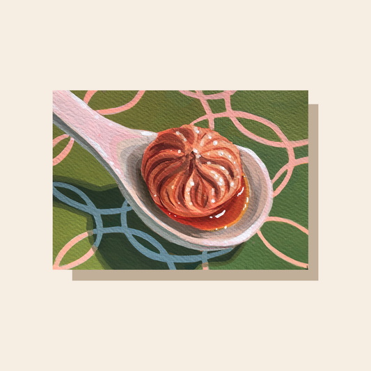 This art print features a soup dumpling sitting in a white ceramic spoon. It rests on a green tablecloth with a circular ring pattern.