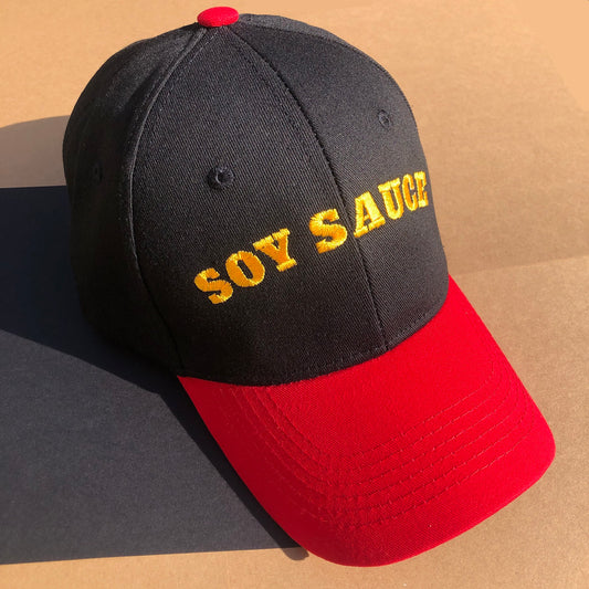A black hat with a red bill is embroider with the words "SOY SAUCE" in yellow thread.