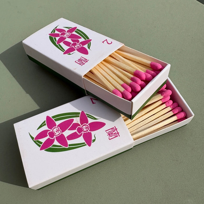 Orchid matchbox with pink matches and floral design on a green background