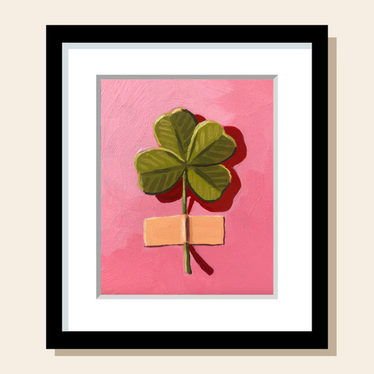This painting art print features a green 4 leaf clover taped to a pink wall with yellow masking tape. The colors are vibrant.